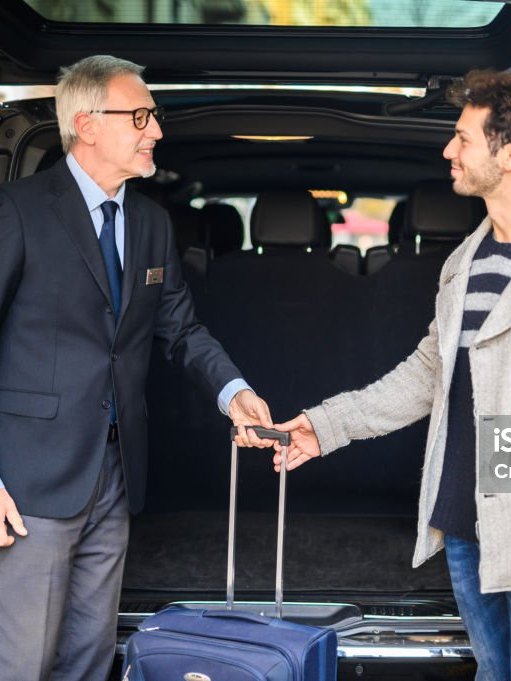 Chauffeur in a suit taking a passenger's suitcase at the open boot of a black car